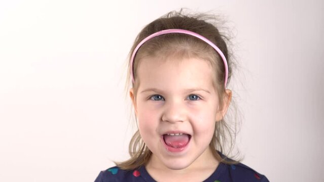 Small girl making a funny expressive grimace face and sticks out tongue. Close-up portrait of joyful cute cheerful toddler girl