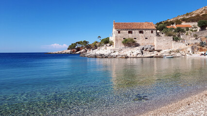 Tranquil scenery of an old stone village by the adriatic sea with crystal clear water reflecting the blue sky, Plaža Dubovica, Hvar, Croatia