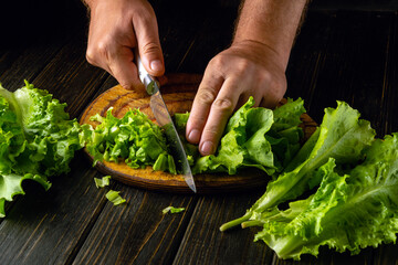 Cutting lettuce leaves with a knife in a man hand to prepare a vegetable salad at home. Advertising space on blackboards