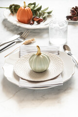 Thanksgiving tablescape on a white marble backdrop with plates, table napkins, and cutlery. 