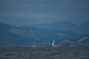 A white ship with a white sail sails the sea on the horizon on a cloudy windy day