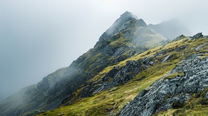 Fototapeta premium Majestic mountain shrouded in mist with rocky slopes and green patches