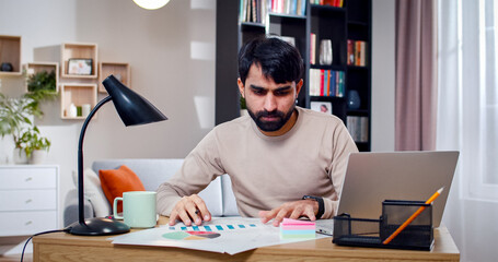 Close up portrait of Arabian male sitting at table draws diagrams on papers. Bearded face man works...