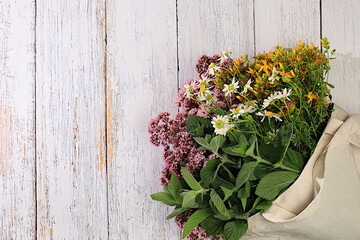 A flower arrangement of wild medicinal herbs on a wooden table in a canvas eco-friendly bag, a bouquet of St. John's wort, oregano, mint, chamomile, a collection of useful herbs for treatment .