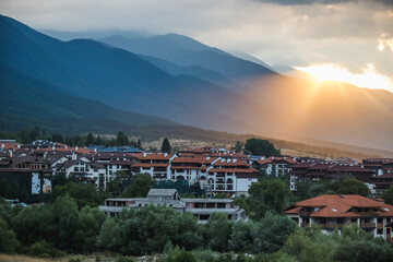 Obraz premium View of Bansko and the surrounding mountains as the setting sun breaks through the clouds, Bulgaria