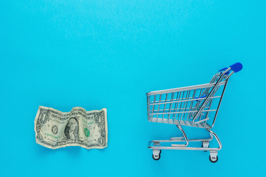 Crumpled dollar bancnote with a shopping cart on blue background. Minimal Coronavirus outbreak. Saving money concept.