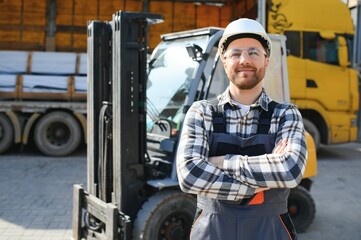 forklift driver in protective vest and forklift standing at warehouse of freight forwarding company, smiling