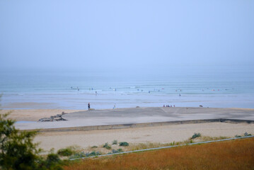 Serene Beach with Surfers and Foggy Horizon - Perfect for Calm and Relaxation