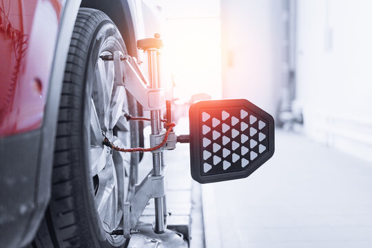 Vehicle inside garage workshop for auto camber fixing work. Closeup car wheel alignment on stand with sensors check in service station.