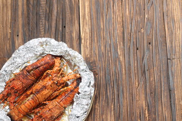 Three buttery baked lobster on a plate with aluminum foil paper sit on top of wooden table....