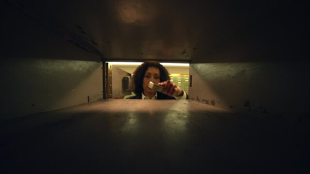 A woman is seen inside a bank vault, carefully examining the safe deposit boxes
