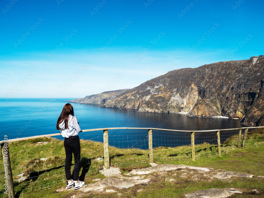 Sticker Young teenager girl exploring beautiful Sliabh Liag, county Donegal, Ireland. Travel and tourism. Warm sunny day. Stunning Irish nature landscape scene in the background.