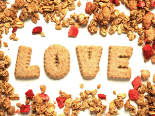 Word love with letters made from cookie on white background framed by granola cereal with dried strawberry. Top down view.