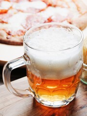 A glass of lager beer in focus. Italian cooked pizza out of focus in the background. Light and airy look.