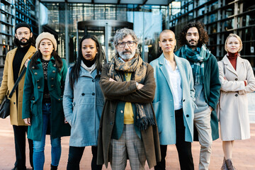 Fototapeta premium Successful professional business people looking at camera outdoors. Senior businessman leading his team, standing together over corporate office building. Teamwork and leadership concept.