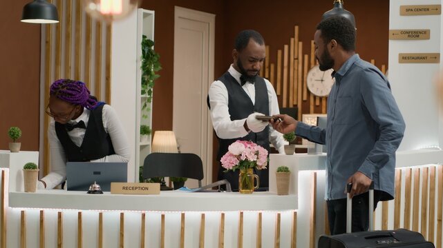 Hotel staff verifying id papers for guest arriving in lobby, preparing to do check in process and sign registration papers with personal information. Tourist on exotic holiday. Handheld shot.