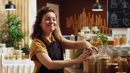 Portrait of smiling zero waste supermarket owner using biodegradable glass containers for its bulk...