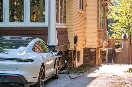 green economy: close up of a high performance electric vehicle connected to a home charging station in a residential driveway