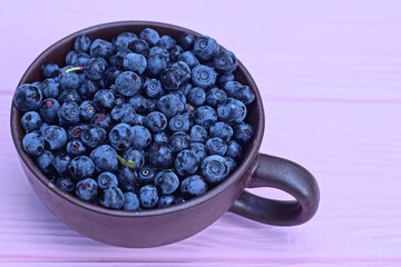 fresh blue blueberries in a brown ceramic cup on a pink wooden table