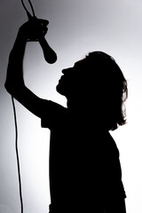 Silhouette of young singer holding wired microphone and singing with emotion.