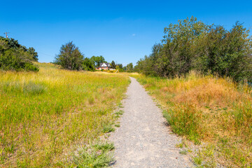 A gravel walking trail leading from a rural country farmhouse in the hills.