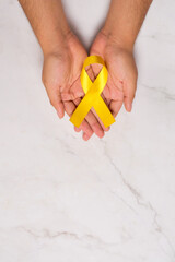 Female hands hold yellow ribbon for Suicide Prevention Day or Childhood Cancer Day, with copyspace