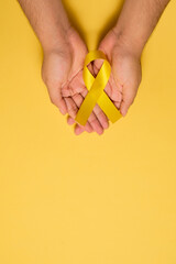 Female hands hold yellow ribbon for Suicide Prevention Day or Childhood Cancer Day, with copyspace