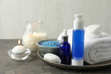 Spa composition. Cosmetic products, terry towel, burning candles and sea salt on gray table against light background