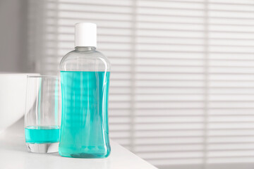 Bottle and glass of mouthwash on white countertop in bathroom, space for text