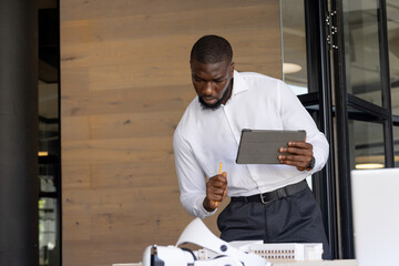 Using tablet and pencil, businessman analyzing architectural model in office