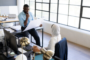 Holding blueprint, businessman discussing project while colleague with coffee listens attentively
