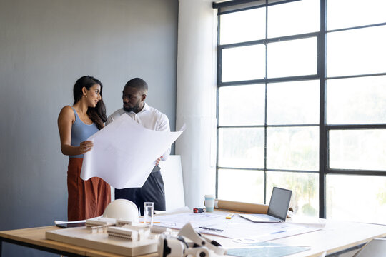 Architects reviewing blueprints in office, discussing project details near window, copy space