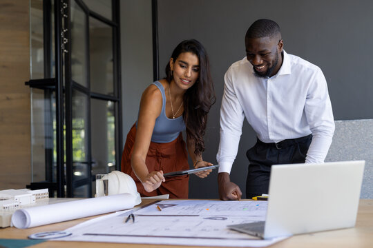 Collaborating on project, colleagues reviewing blueprints and using tablet in office