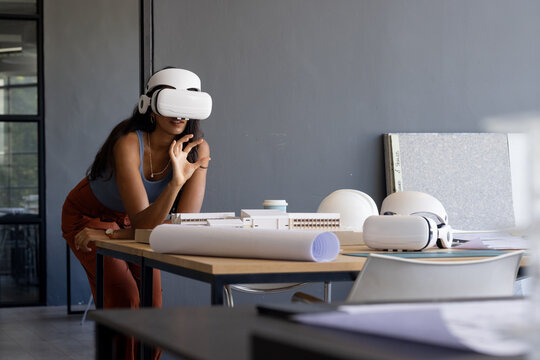 Using VR headset, woman exploring architectural model in modern office workspace, copy space