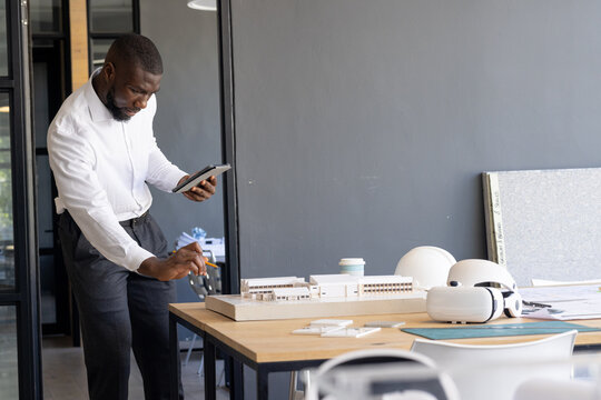 Architect examining scale model and using tablet in modern office, copy space