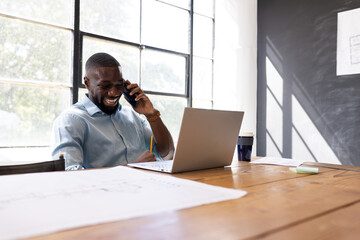 Talking on phone and using laptop, man working in modern office setting