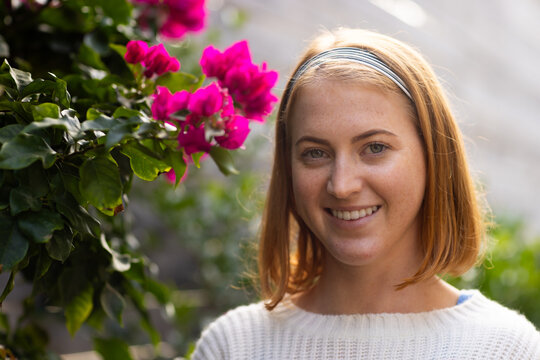 Smiling woman with headband standing next to vibrant pink flowers outdoors, copy space