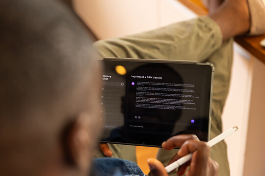 Using AI chatbot on tablet and stylus, man reading about implementing CRM system at home
