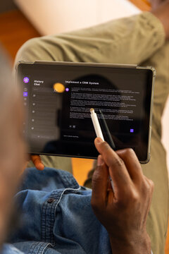 Using stylus on AI chatbot on tablet, man reading about implementing CRM system at home