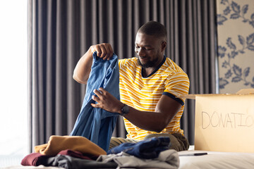 Sorting clothes for donation, man smiling and organizing items in bedroom
