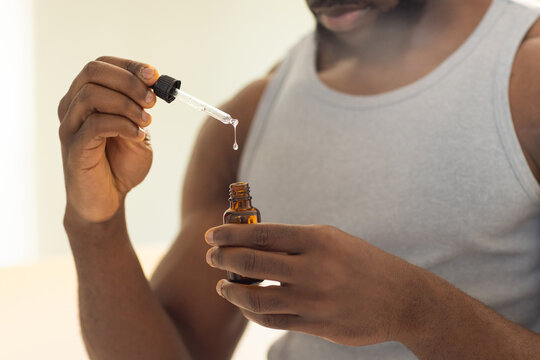 African American man using dropper bottle for skincare routine at home