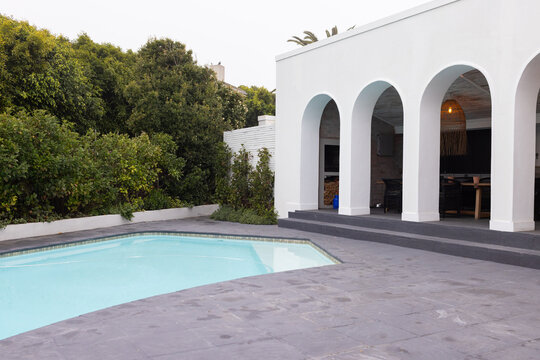 Modern home with swimming pool and patio, surrounded by lush greenery, copy space