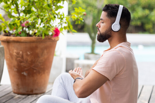 Meditating outdoors, man wearing headphones and sitting peacefully on wooden deck, copy space