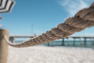 Close up of rope with the beach and a jetty in the background
