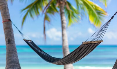 Obraz premium Peaceful tropical beach scene with a hammock hanging between two palm trees overlooking the turquoise ocean and clear blue sky.