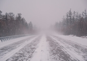 Snow-covered highway through forest during intense winter storm in daytime