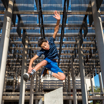 A fit preteen boy practices extreme parkour, leaping off a city structure and flying through the air