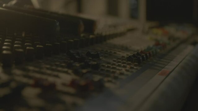 Person hand adjusts levers on DJ console in semi-dark studio closeup. Musician mixes tracks on control panel in nightclub. Audio equipment