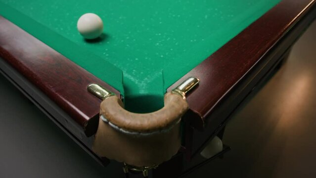 Slowmo of white billiard ball falling into hole on green pool table during game