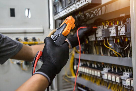 Electrician holding electrical measuring tool meter on panel circuit breaker power electricity switchboard system cabinet for repairing or safety service maintenance and electric cable wiring check.